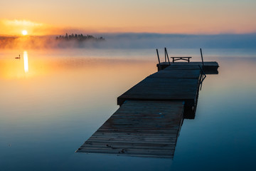 Wooden jetty floating on a still lake at sunrise, Sweden.