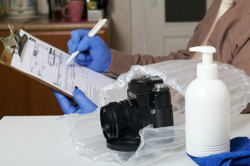 Fototapeta na wymiar Parcel delivery during self-isolation. A man in rubber gloves signs a package delivery form. Next to him in a bubble pack was a camera sent to him. Visible spray with a disinfectant and a napkin.