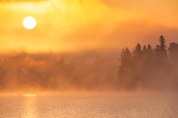 Sun rising above forest and misty lake, Sweden.