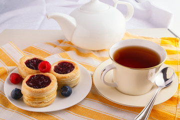 Cup of black tea with danish pastry cake with cranberry jam and fresh blueberry and raspberry on the table. Sunny breakfast.