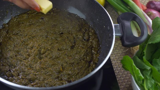 Closeup shot of woman hands adding butter in delicious Punjabi cuisine - Saag. Traditional Indian Food. Pan shot of an Indian female putting butter while cooking Sarson ka saag in a nonstick pan - ...