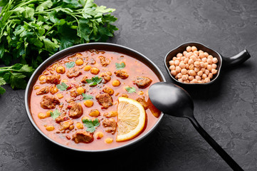 Moroccan Harira Soup in black bowl at dark slate bakcground. Harira is Moroccan Cuisine dish with lamb or beef meat, chickpeas, lentils, tomatoes and ciliantro. Ramadan Iftar Food. Copy space