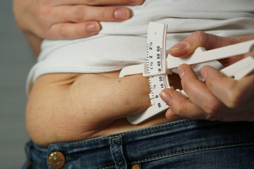 A woman in a white T-shirt and navy blue jeans measures the level of body fat with a special device, closeup.