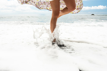 woman standing on one leg by beach with water splashing on legs