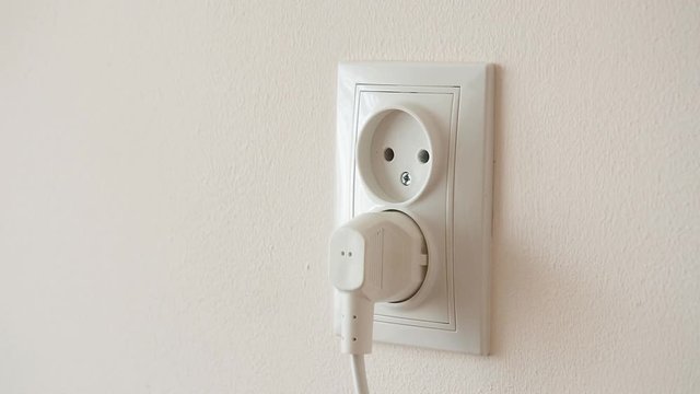 Female hand Inserts plug Into electrical socket on a light wall