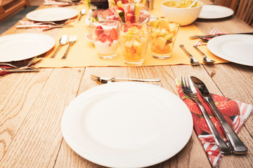real set breakfast table with small glass bowls full of fruits and fish, yellow tablecloth, silver cutlery, white plates on wooden table