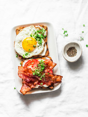 Delicious breakfast - sandwiches with cream cheese, fried egg, tomatoes, bacon on a light background, top view