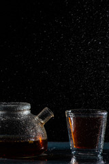 herbal sea black tea in a transparent teapot and in a transparent glass with a double bottom on a black background with splashes of water