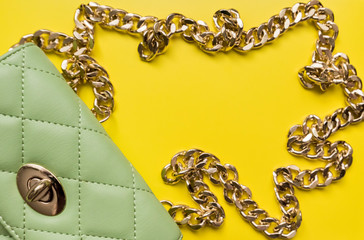 Woman's fashionable stitched green clutch with golden details made of smooth shining patent leather isolated on yellow background. Logos removed. Elegant woman bag.