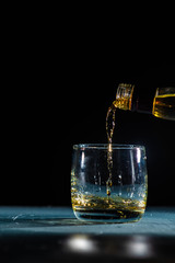 whiskey pouring from a bottle into a glass on a black background with bright highlights