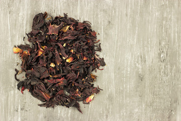 Pile of dried red tea leaves, karkade on a grey background, copy space
