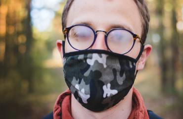 A young white man in a forest wearing a moro pattern cotton mask during a walk with fogging up, fog...