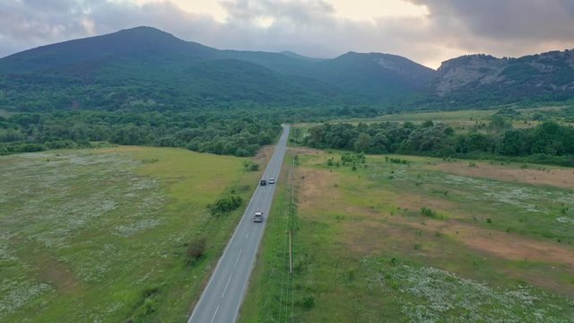 Drone tracking shots vehicles driving along asphalt road as one car performs overtaking maneuver in mountain valley. Cinematic aerial automotive video footage serves as background for design element.