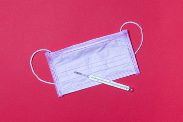pink medicine facemask and mercury thermometer on red background
