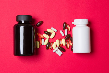 black and white vitamin container and pills on red colored paper background