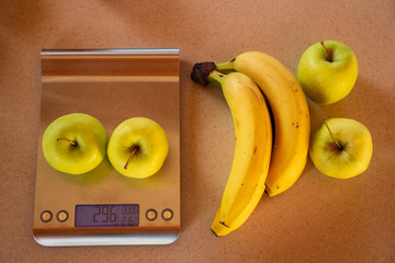 apples on a digital kitchen scale and beside are bananas and apples