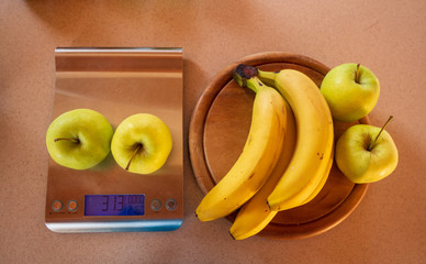 apples on a digital kitchen scale and beside are bananas and apples