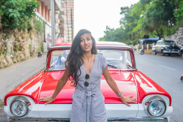 Fototapeta na wymiar Young indian woman happy in front of red car in Havana