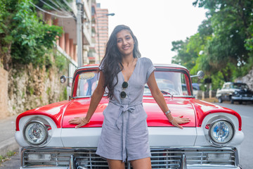Young indian woman happy in front of red car in Havana