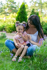 Fototapeta premium vertical portrait of a thirty five year old woman with three year old daughter against the background of a summer park