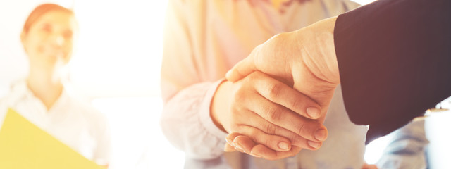 Business people shaking hands. Women finishing successful meeting. Three persons. Intentional sun glare. Wide screen panoramic
