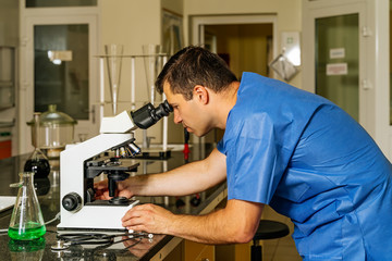 Male doctor or lab technician checking or researching covid 19 virus samples under microscope to help with discovery of coronavirus vaccination