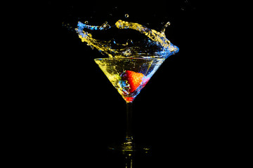 martini cocktail with colored splash in blue and yellow with red strawberry