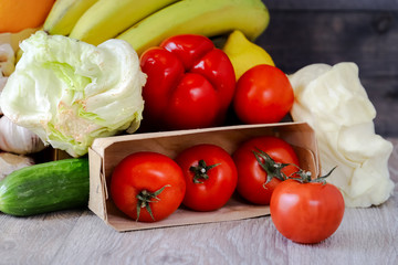 Close-up in a box of tomatoes, next to the table are cucumber, garlic, Iceberg salad, large red peppers, bananas, oranges.