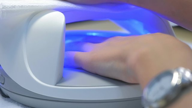 Woman is drying nails with shellac in UV lamp, clouseup view. Polymerization process to gel polish. Beauty industry concept. Nails hygiene and care.