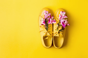 Pair of yellow sneakers and flower buds on yellow background. Spring summer fashion concept, copy space