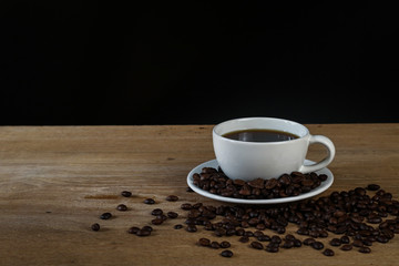White coffee cup and coffee beans on wooden table with copyspace for text. Selective focus.