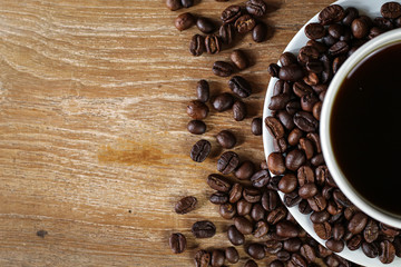 White coffee cup and coffee beans on wooden table with copyspace for text. Selective focus.