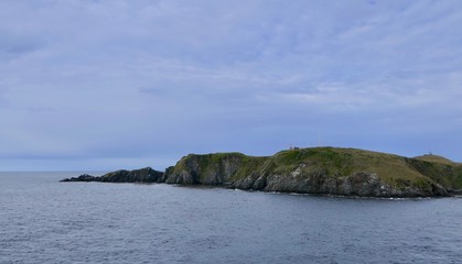 Cape horn gras landscape and cliff with lighthouse in background and dark, stormy, clouds, Chile, Cape Horn
