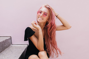 Amazing european woman chilling on stairs after walk around town and smiling to camera. Pink-haired inspired girl in dress posing on the steps.