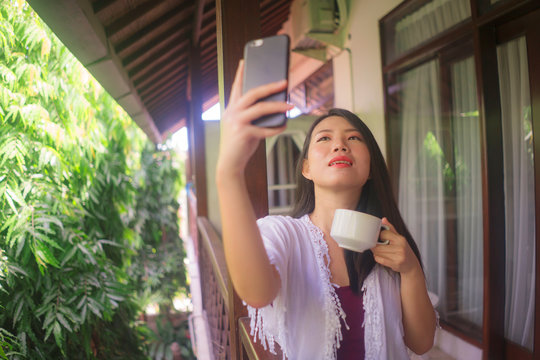  Young Beautiful And Happy Asian Korean Woman Having Morning Coffee Taking Selfie With Mobile Phone For Social Media At Home Terrace Or Hotel Room Balcony