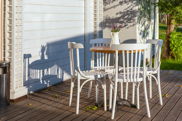 An empty table of an outdoor cafe with white painted chairs on a wooden floor