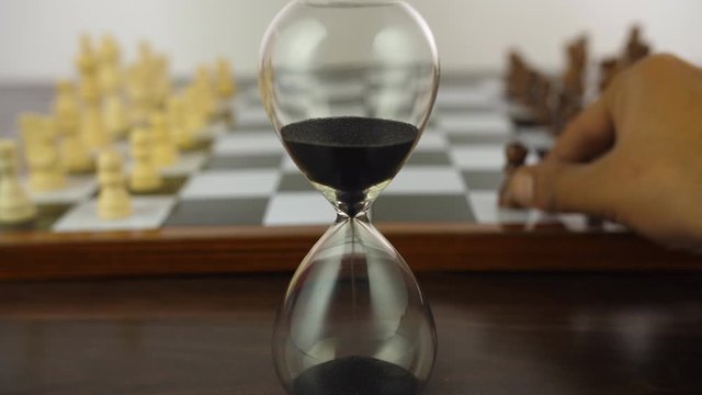 Checkered board with black and white chess pieces against the white background. Closeup shot of hands playing chess  a strategy board game  next to a glass sand clock during leisure time in India