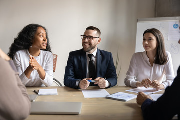Smiling multiracial businesspeople brainstorm at desk in boardroom discuss financial ideas together, happy employees talk with business partners at office meeting, partnership, collaboration concept