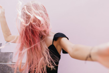 Wonderful long-haired woman in black dress fooling around during studio photoshoot. Indoor portrait of emotional girl with pink hair expressing happiness and dancing.