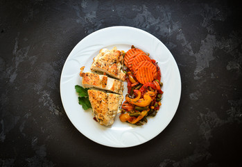 Baked chicken breast with vegetables. Chicken breast, asparagus, carrots, in a white plate. Top view. Dark background. Free space for text.