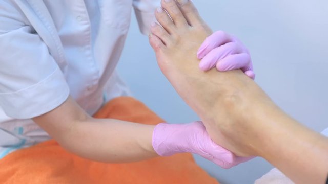 Pedicurist woman doing foot massage using cream, cosmetology procedure in beauty salon, closeup foot. Doctor beautician making massage gor young woman, hands closeup.