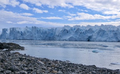 Glacier front with stone beach landscape in Antarctica, blue cloudy sky, Stonington Island