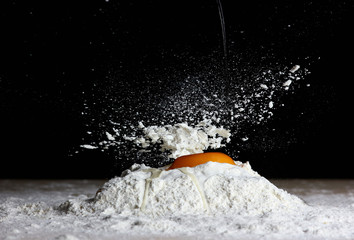 kitchen process on a dark background with an egg falling on the flour when preparing the dough