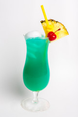 green alcohol cocktail top with coconut decorated with pineapple and red cherry in tall glass isolated on white