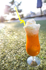 orange thai milk tea with ice top with whipped cream served in tall glass and straw on a green grass