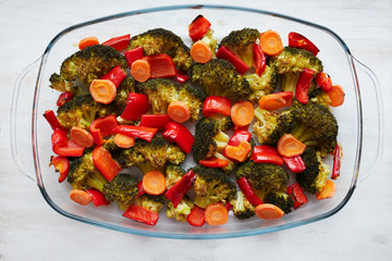 A mix of baked broccoli, bell pepper (paprika) and carrot with a heart made from a carrot's slice on top. Vegetables in the glass dish on the white wooden table
