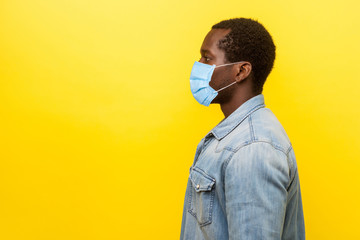 Profile portrait of serious young man with surgical medical mask looking left side with calm confident expression, blank copy space for text. indoor studio shot isolated on yellow background