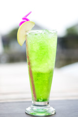 green apple juice drink in a tall glass decorated with sliced green apple
