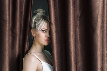 Obraz premium Sexy young blonde looking out from behind the curtains.