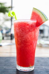 red watermelon smoothie in a tall glass decorated with a piece of watermelon